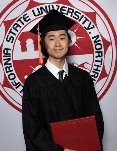 Sam Lee standing in front of the California State University, Northridge sign in a cap and gown, holding his diploma.