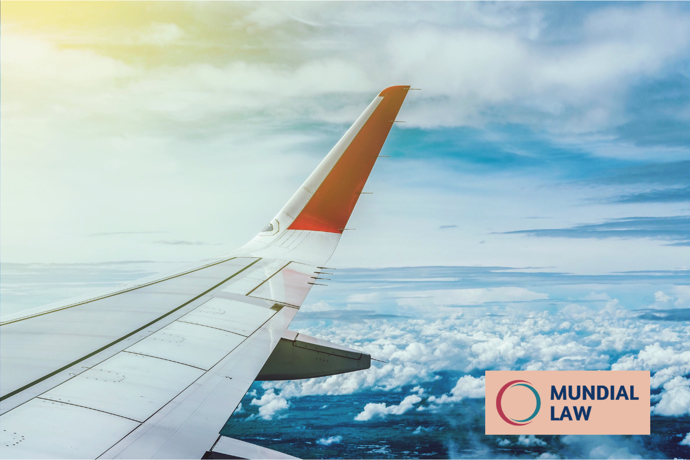 Image of airplane wing in the sky above the clouds with Mundial Law logo in corner.